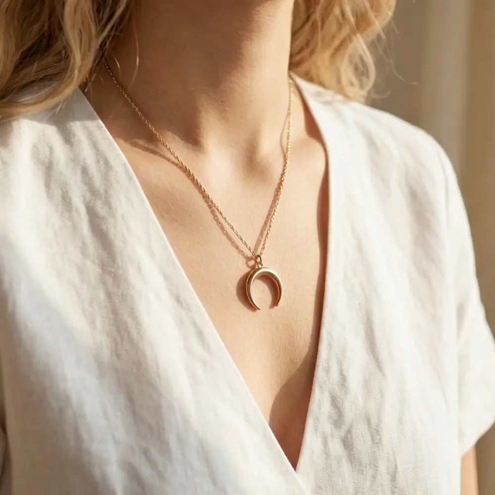Gold necklace with a crescent moon pendant worn by a person in a white top.